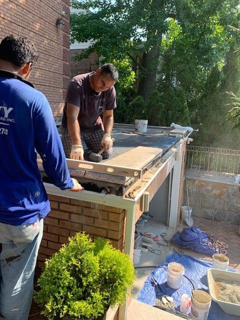 Two men are working on a brick wall outside of a house.