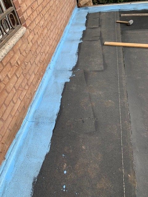 A black roof with a blue border is being installed on a brick building.