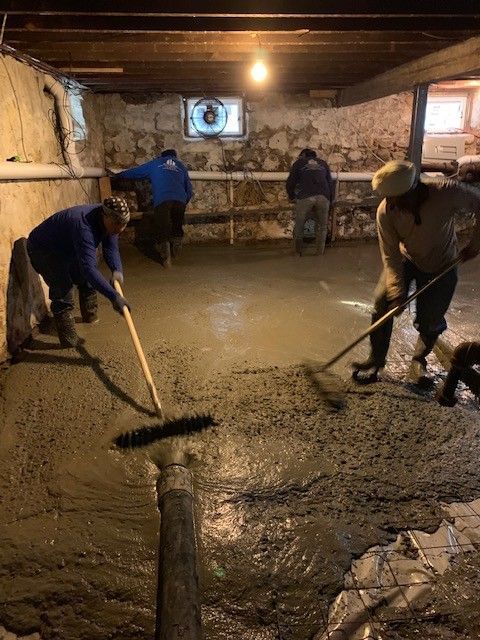 A group of men are working on a concrete floor in a basement.