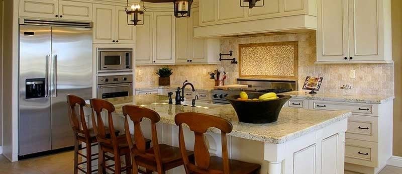 A kitchen with white cabinets and stainless steel appliances and a large island with a bowl of fruit on it.