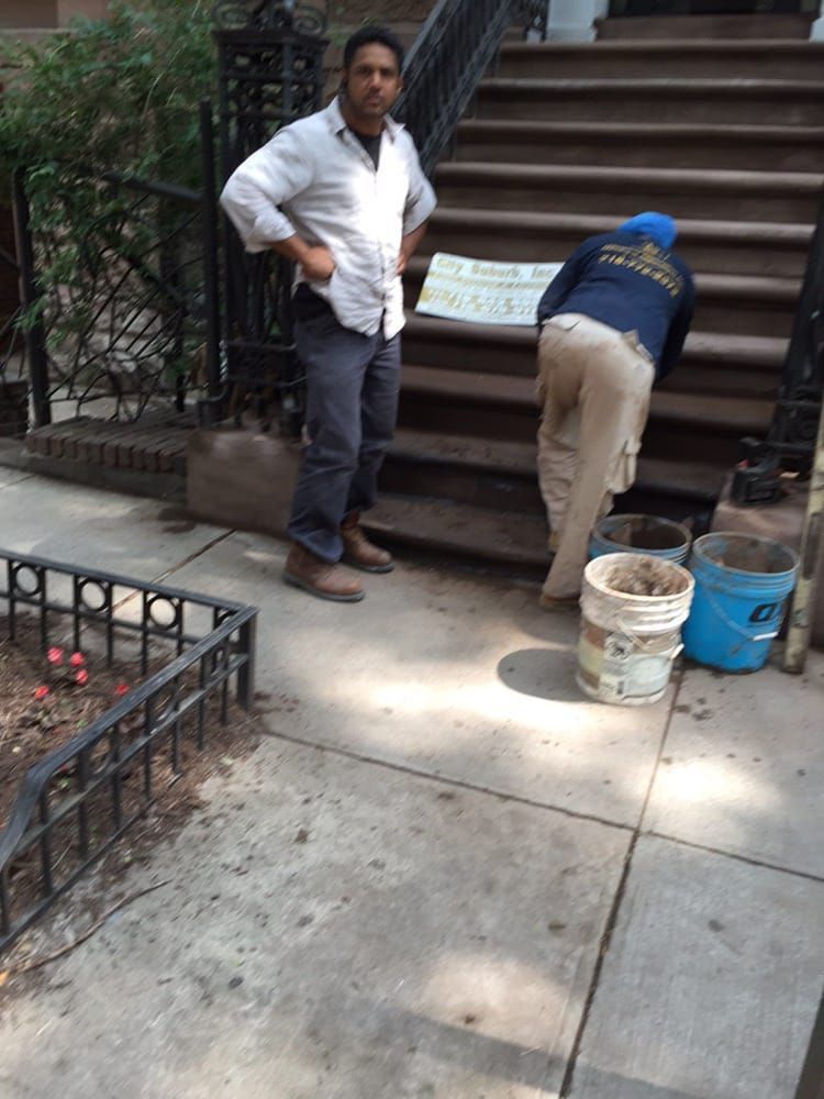 A man is standing on a sidewalk next to a set of stairs.