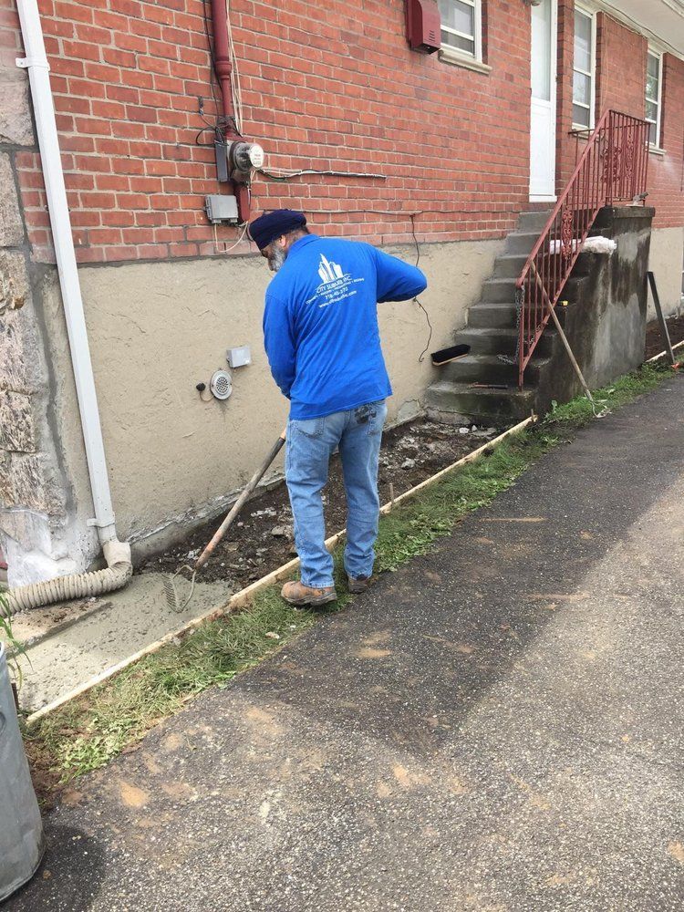A man in a blue shirt is standing in front of a brick building.