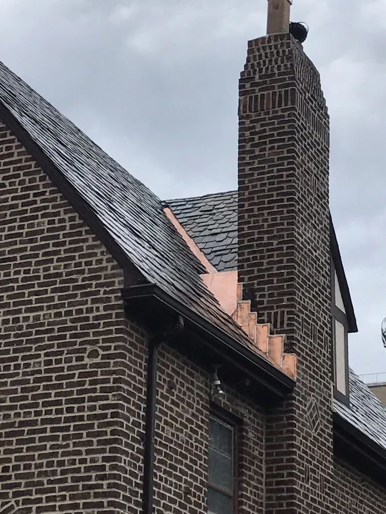 Brick building with slate roof, copper flashing, and chimney against a cloudy sky.