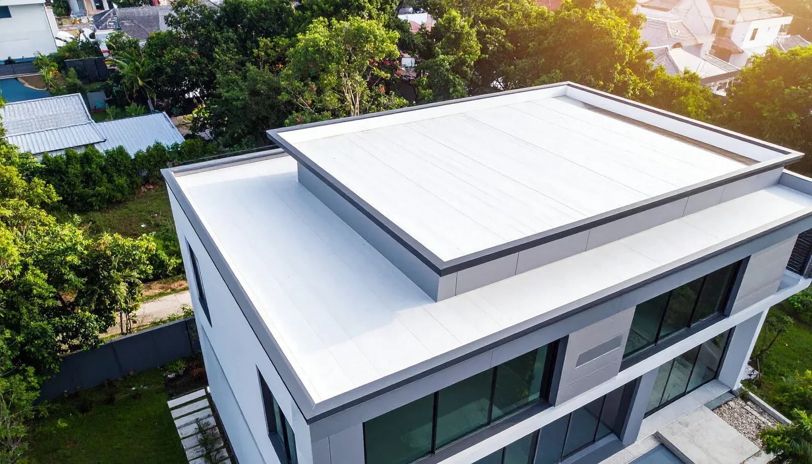 Modern white house with a flat roof and rooftop terrace, viewed from above amid green trees.