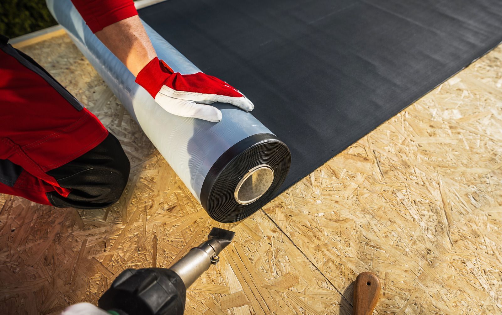 Roofing worker using a heat gun to seal black membrane on plywood roof deck