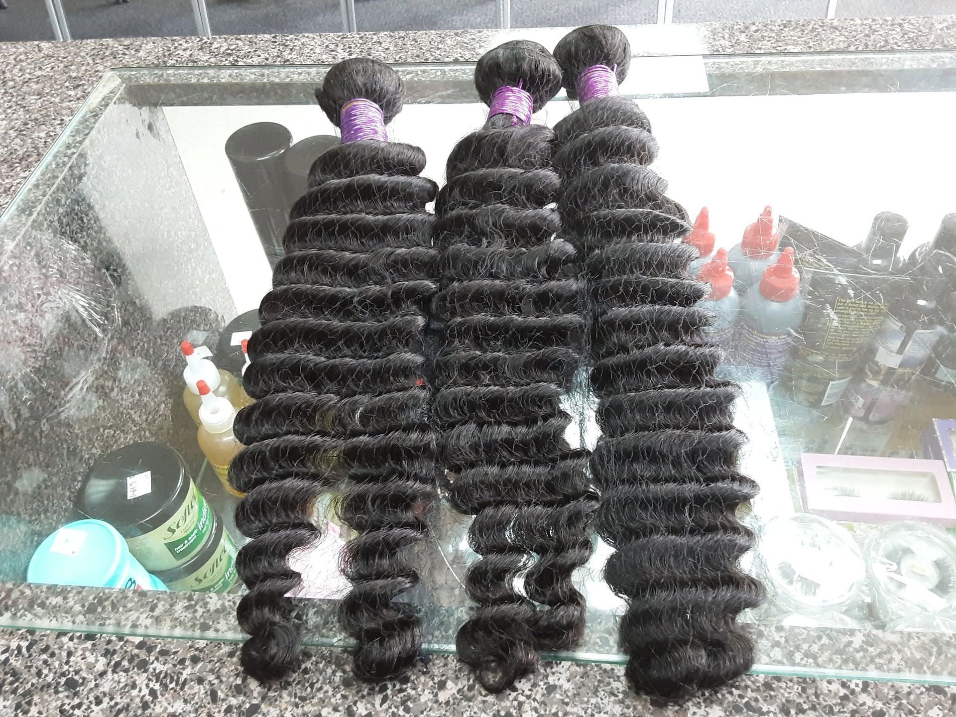 Three long black braided hair extensions with purple bands, displayed on a table among hair products.