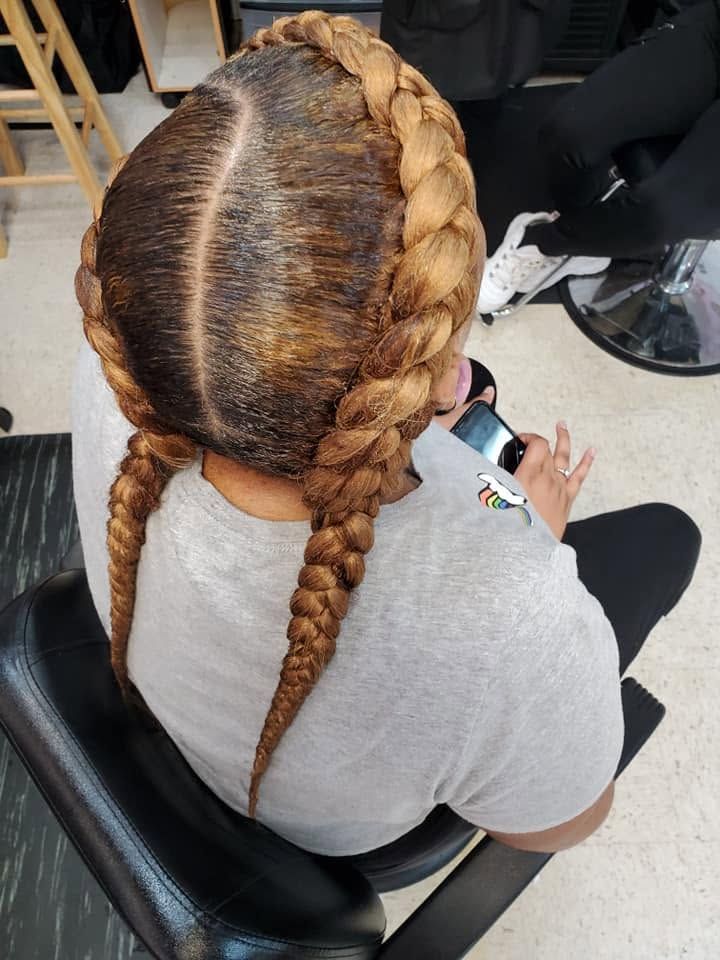 Two braided pigtails on a seated person, viewed from above in a salon chair