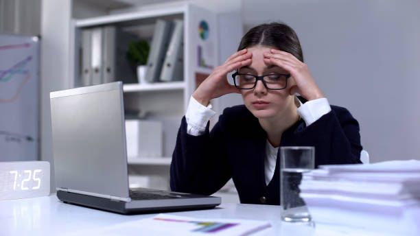 A woman is sitting at a desk with a laptop and a glass of water.