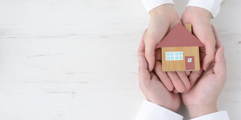 Two people are holding a small house in their hands.