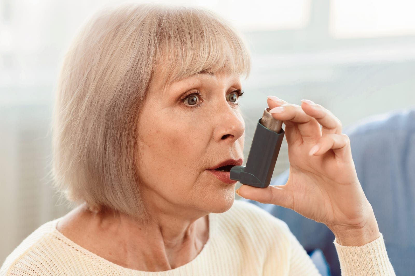 An elderly woman is using an inhaler to treat her asthma.