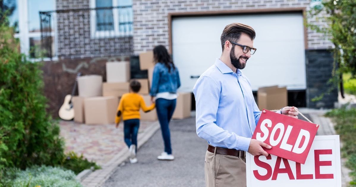 A man is holding a sold sign in front of a house.