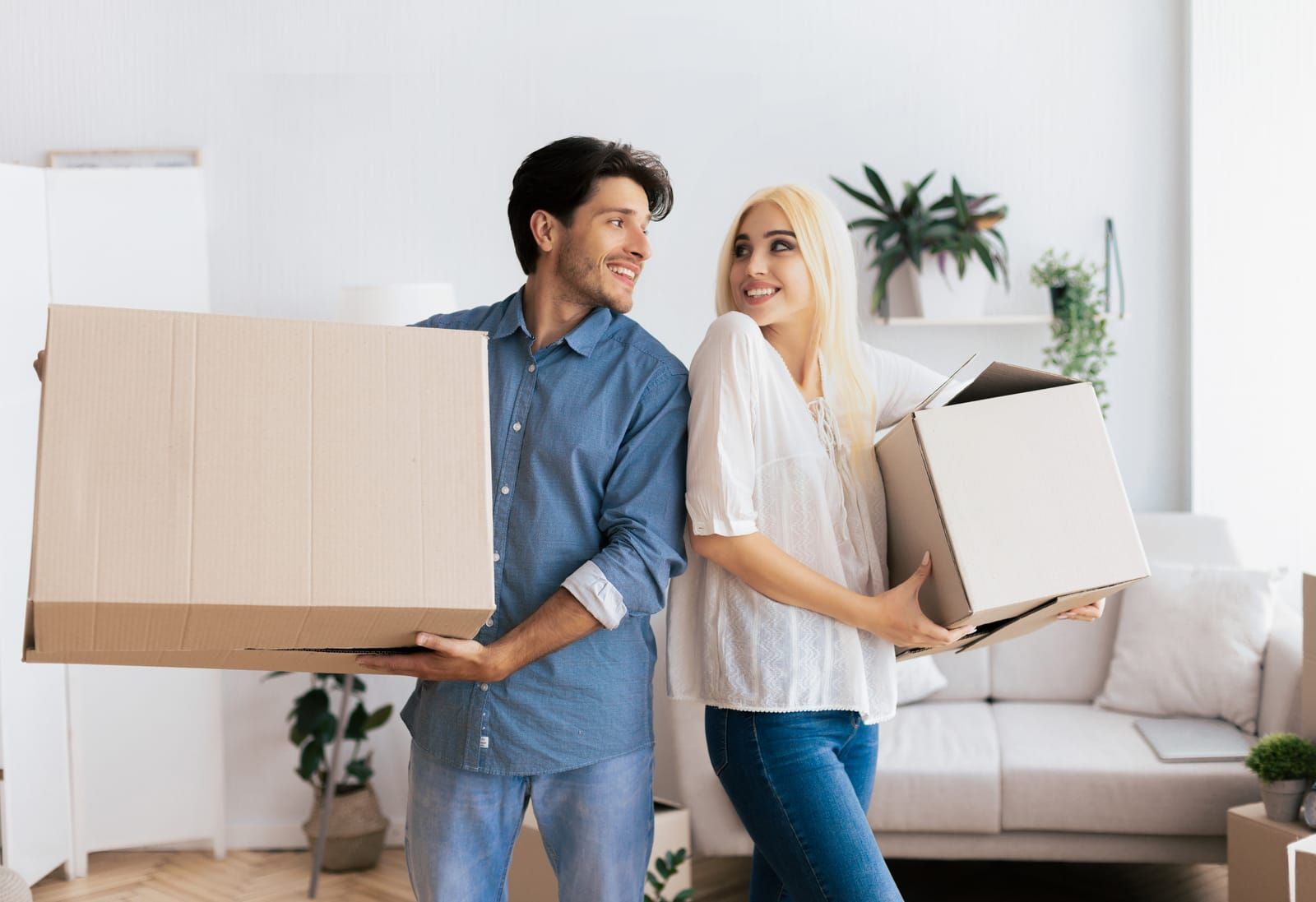 A man and a woman are holding cardboard boxes in a living room.
