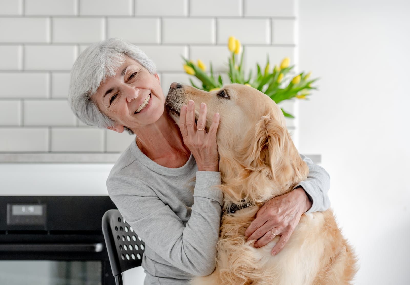 An elderly woman is hugging a dog in a kitchen