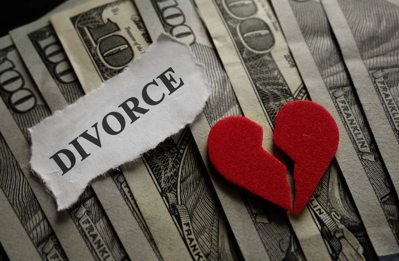 A broken heart is sitting on top of a pile of money next to a piece of paper that says divorce.