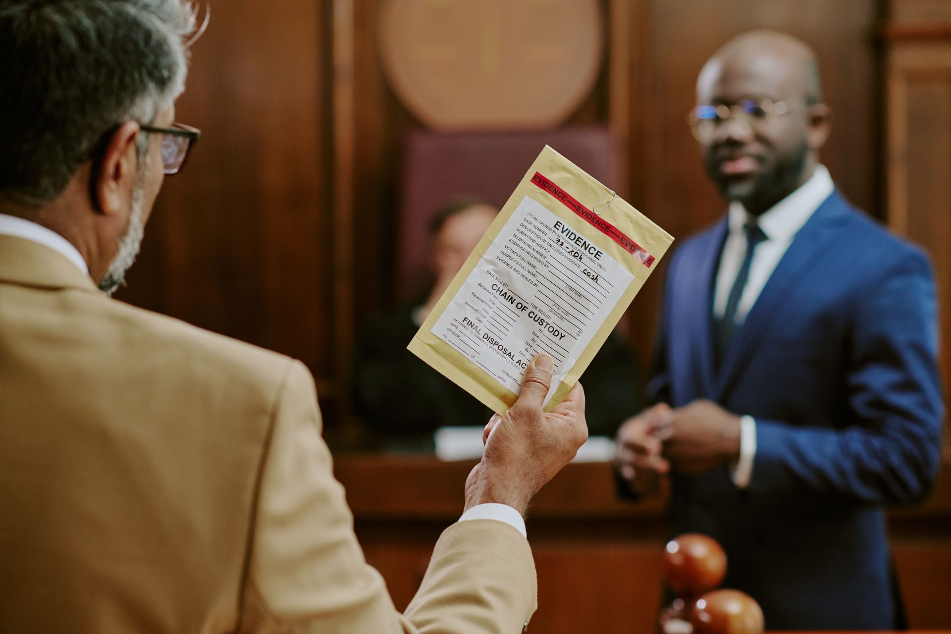 A solicitor is holding an evidence bag while looking at a lawyer and a judge in the background.