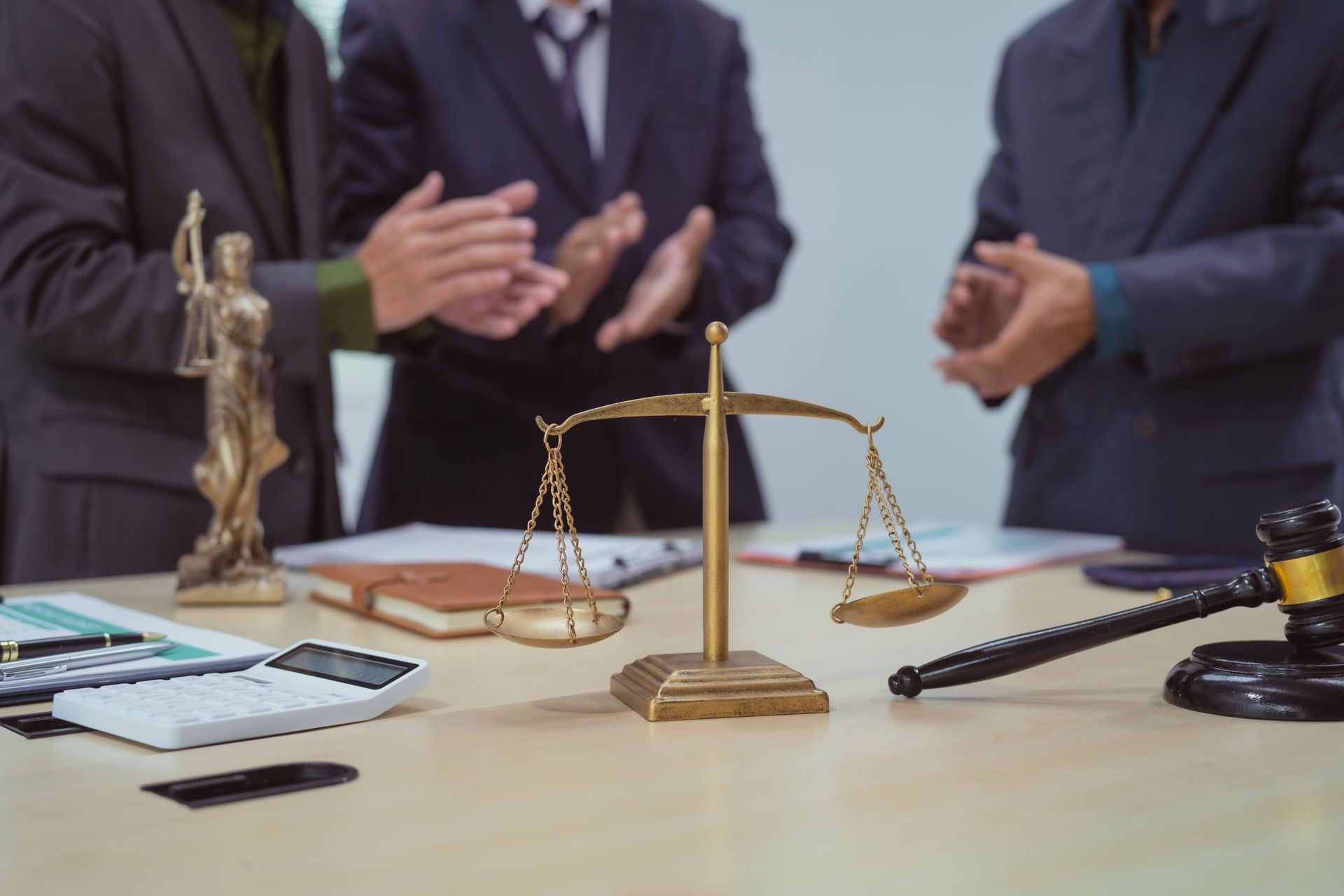 Three lawyers clapping over a table with a gavel, scales of justice, and a Lady Justice statue. Three lawyers clapping over a table with a gavel, scales of justice, and a Lady Justice statue.