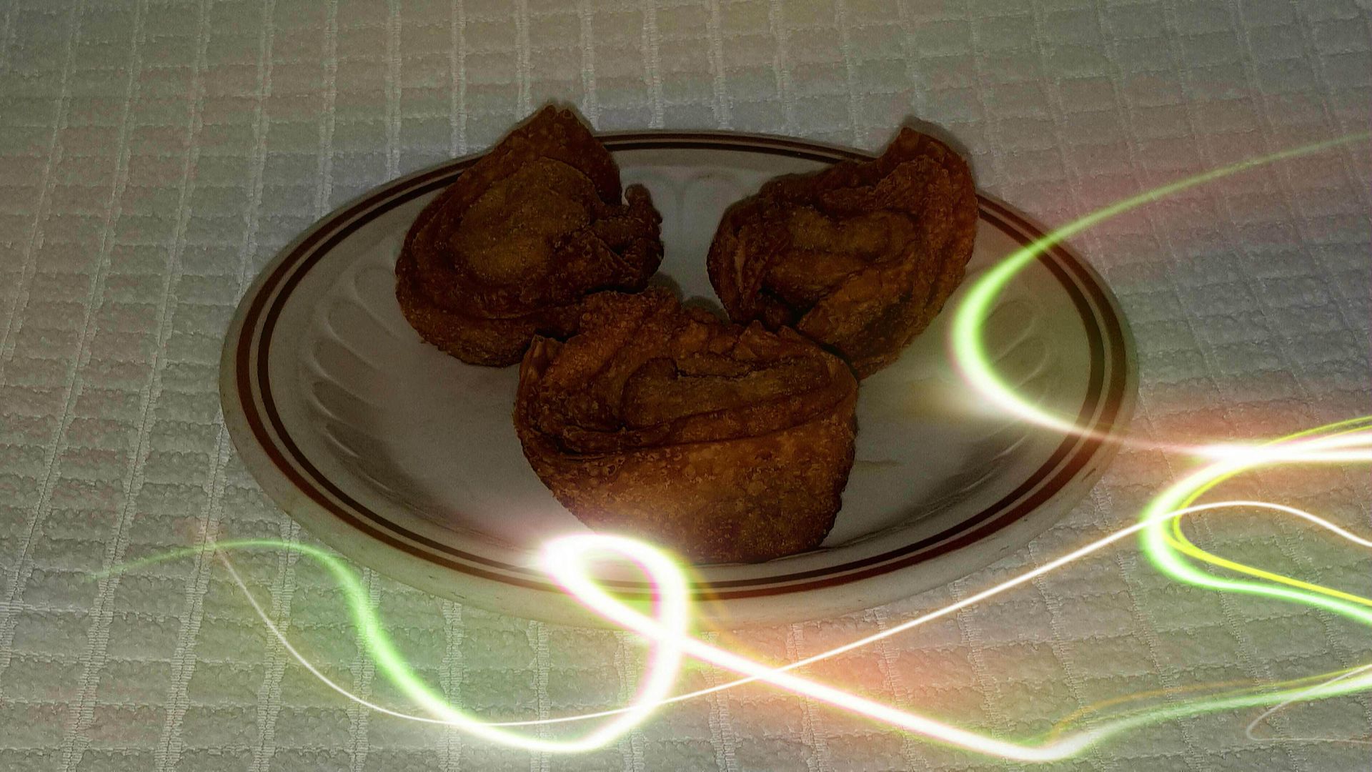 Three dark muffins on a plate with brown trim, sitting on a white checkered surface, with light streaks.