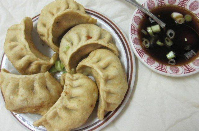 A plate of Potstickers next to a bowl of dipping sauce.