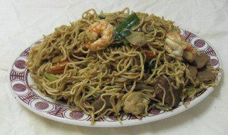 Noodles with shrimp, meat, and vegetables on a patterned plate.