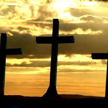Three crosses silhouetted against a golden sunset with cloudy sky.