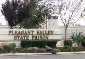 Pleasant Valley State Prison sign with a guard tower and building in the background.