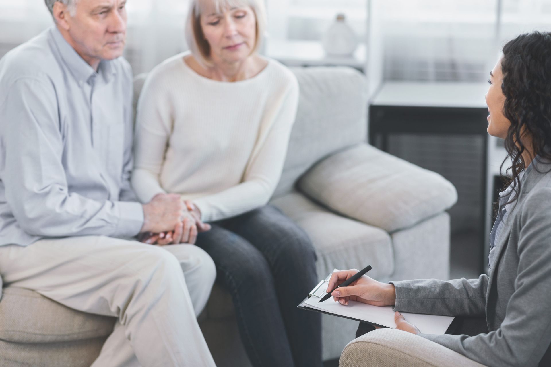 Counselor taking notes while meeting with a couple on a gray sofa