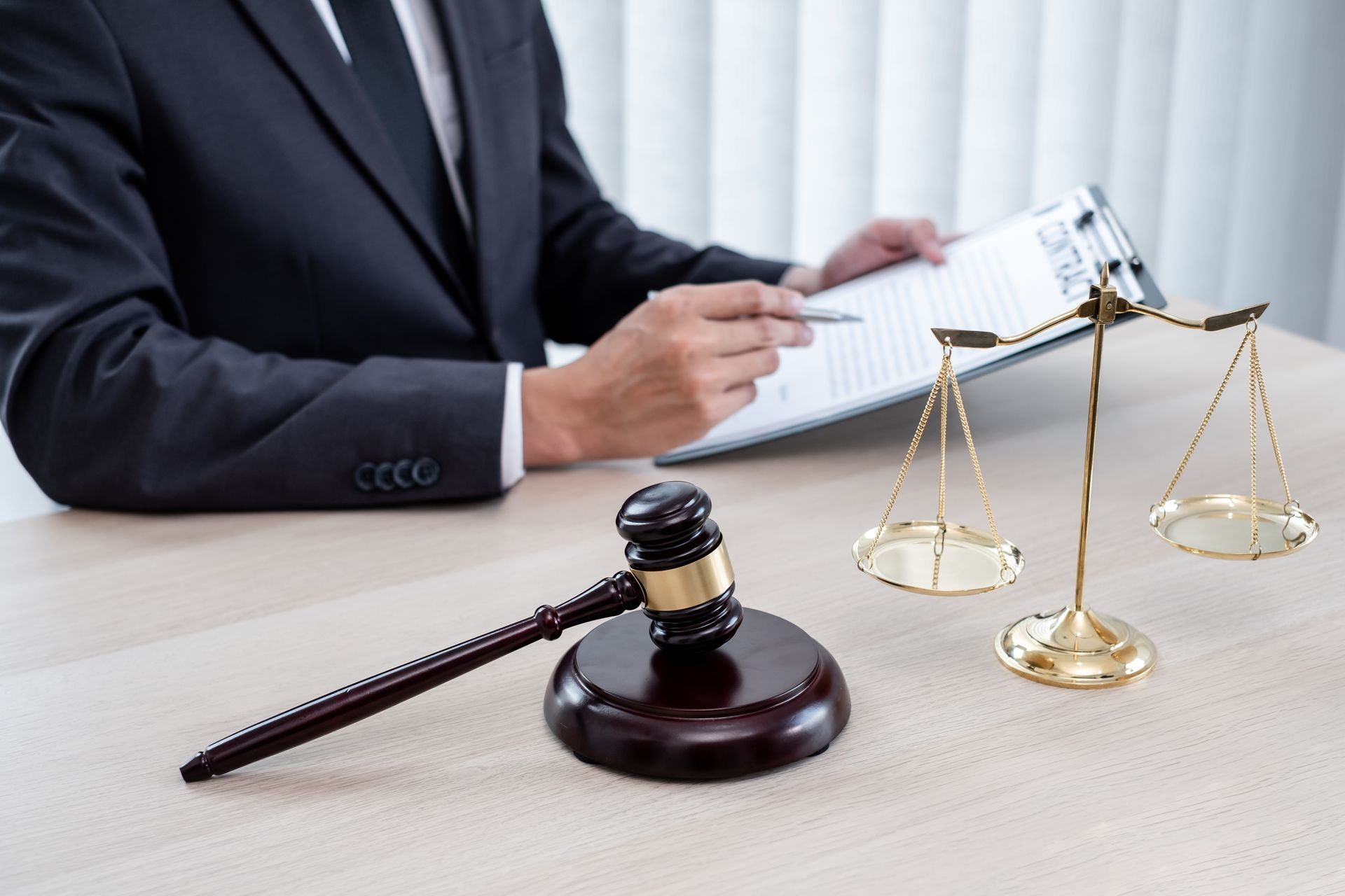 Gavel and scales of justice on desk, lawyer in suit reviewing documents.