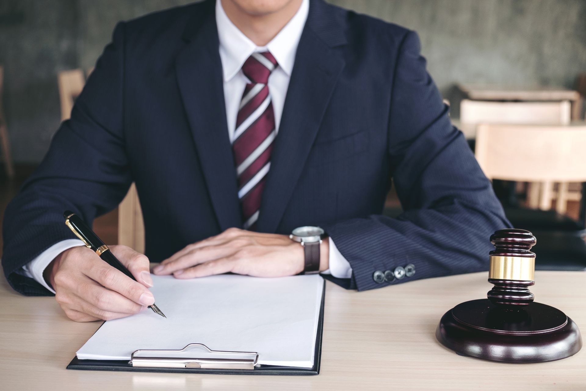 Man in suit writing on paper with gavel on desk.