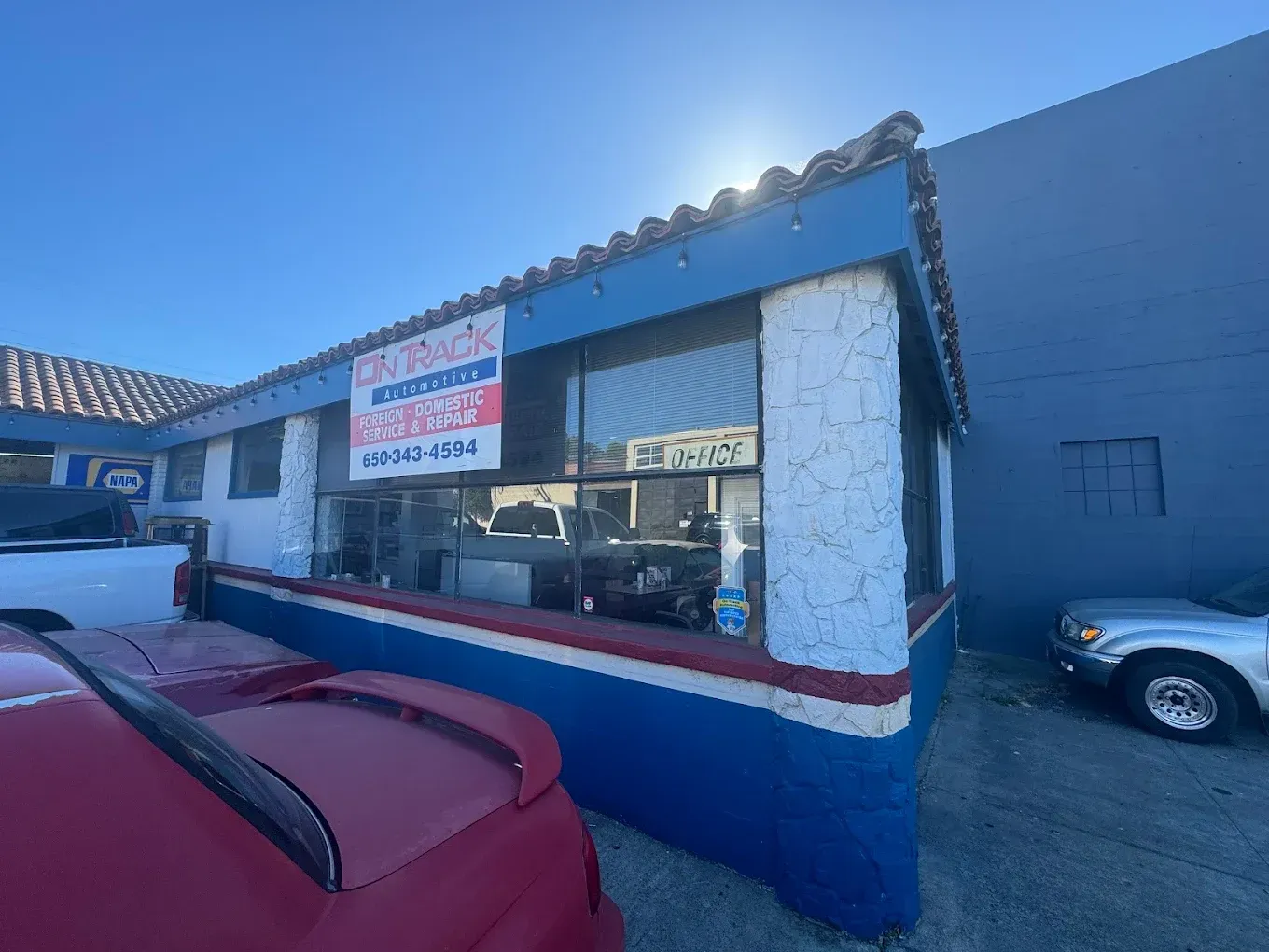 Small storefront with a red, white, and blue facade, parked cars, and a sign in the window.