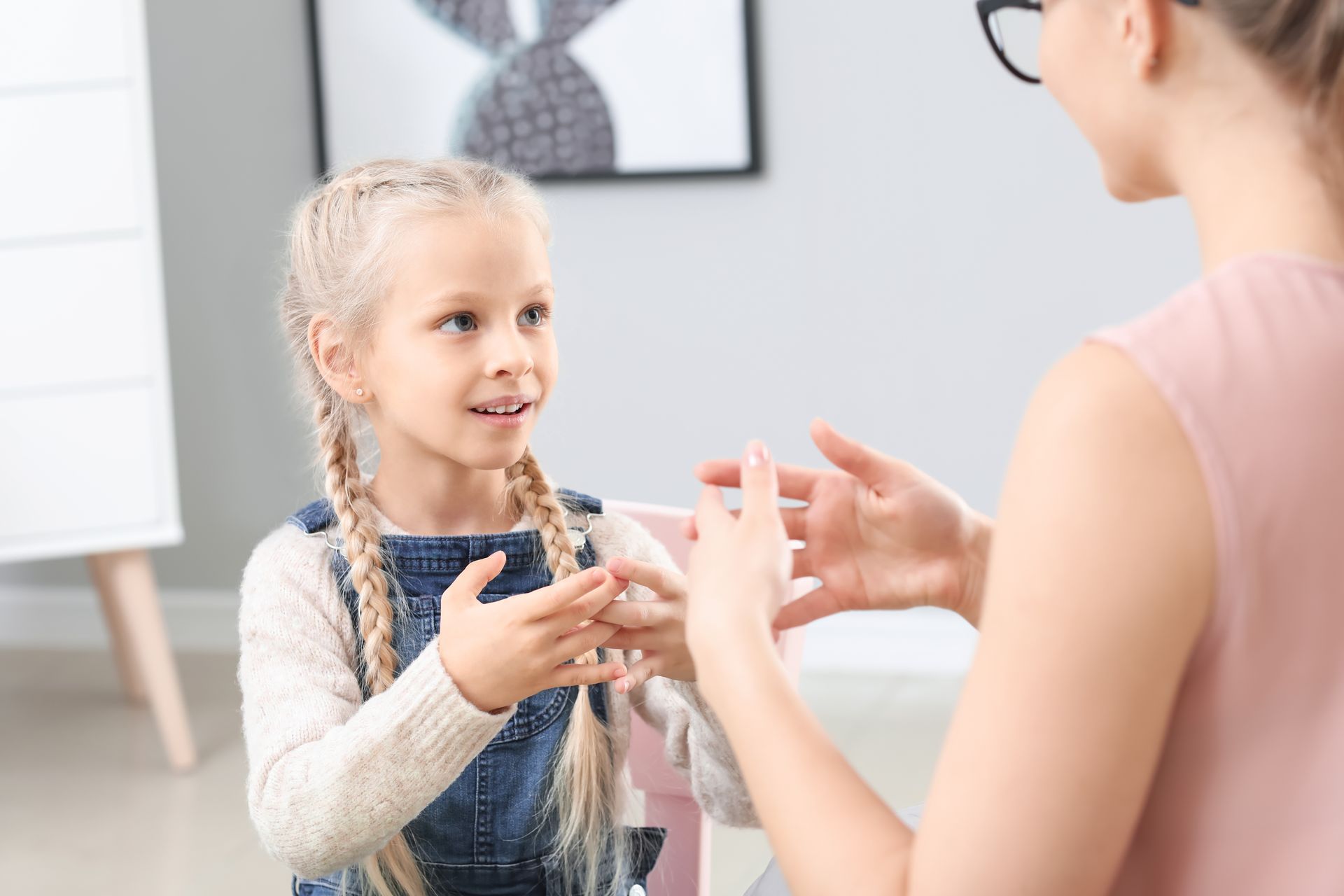 Two people exchanging a small object in a bright room, with a child smiling and looking up at an adult.