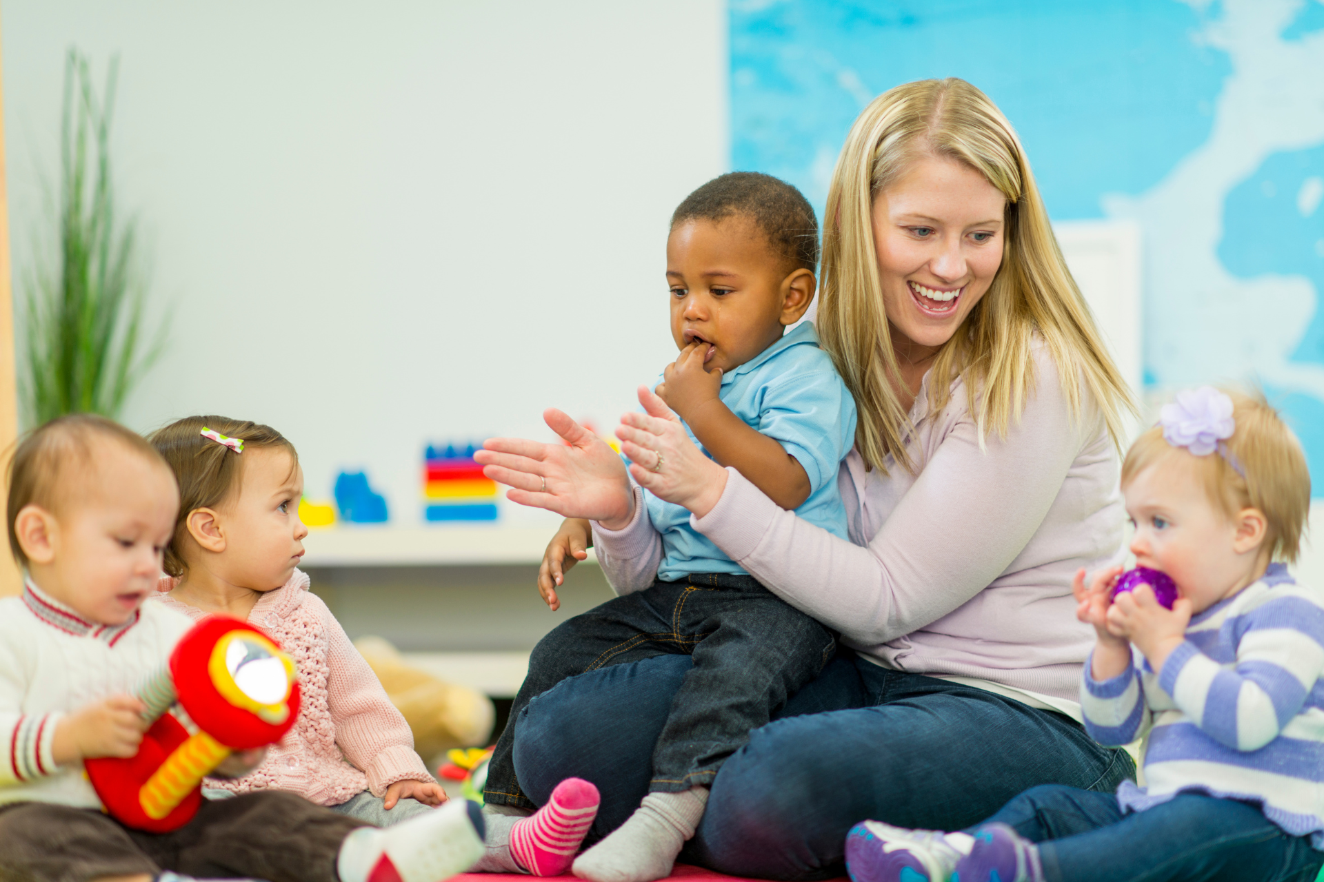 Teacher sitting on the floor with three toddlers in a bright classroom, playing with toys