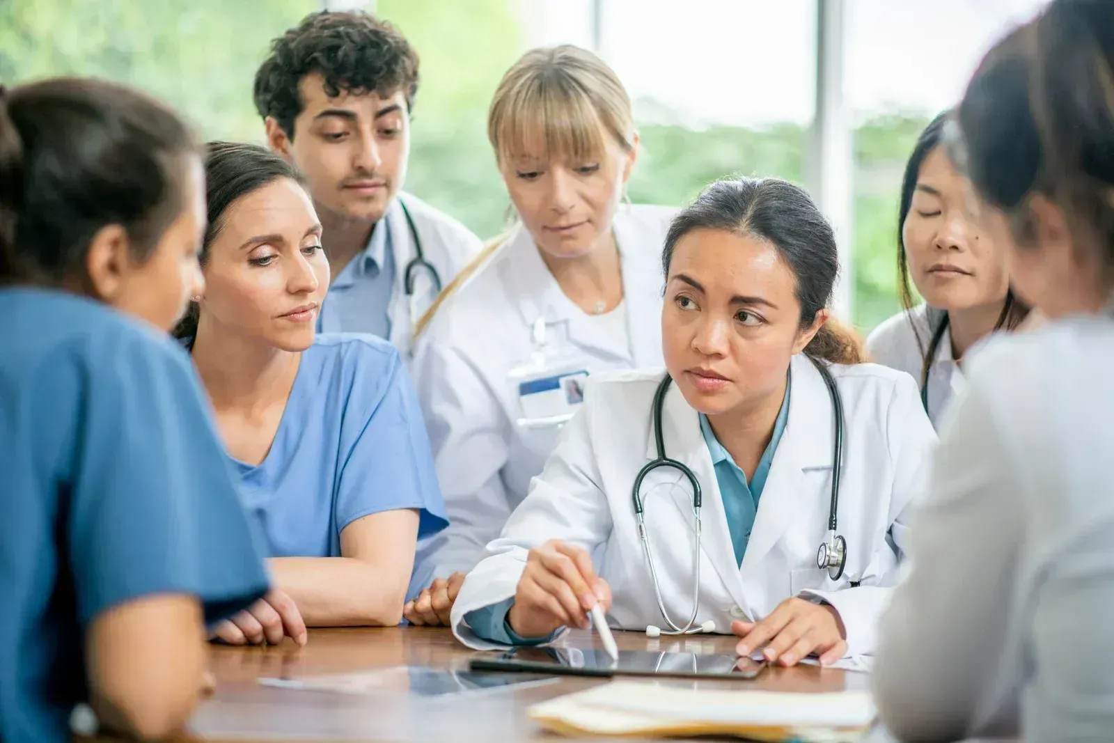 Medical team in discussion around a table, with a doctor taking notes during a collaborative meeting.
