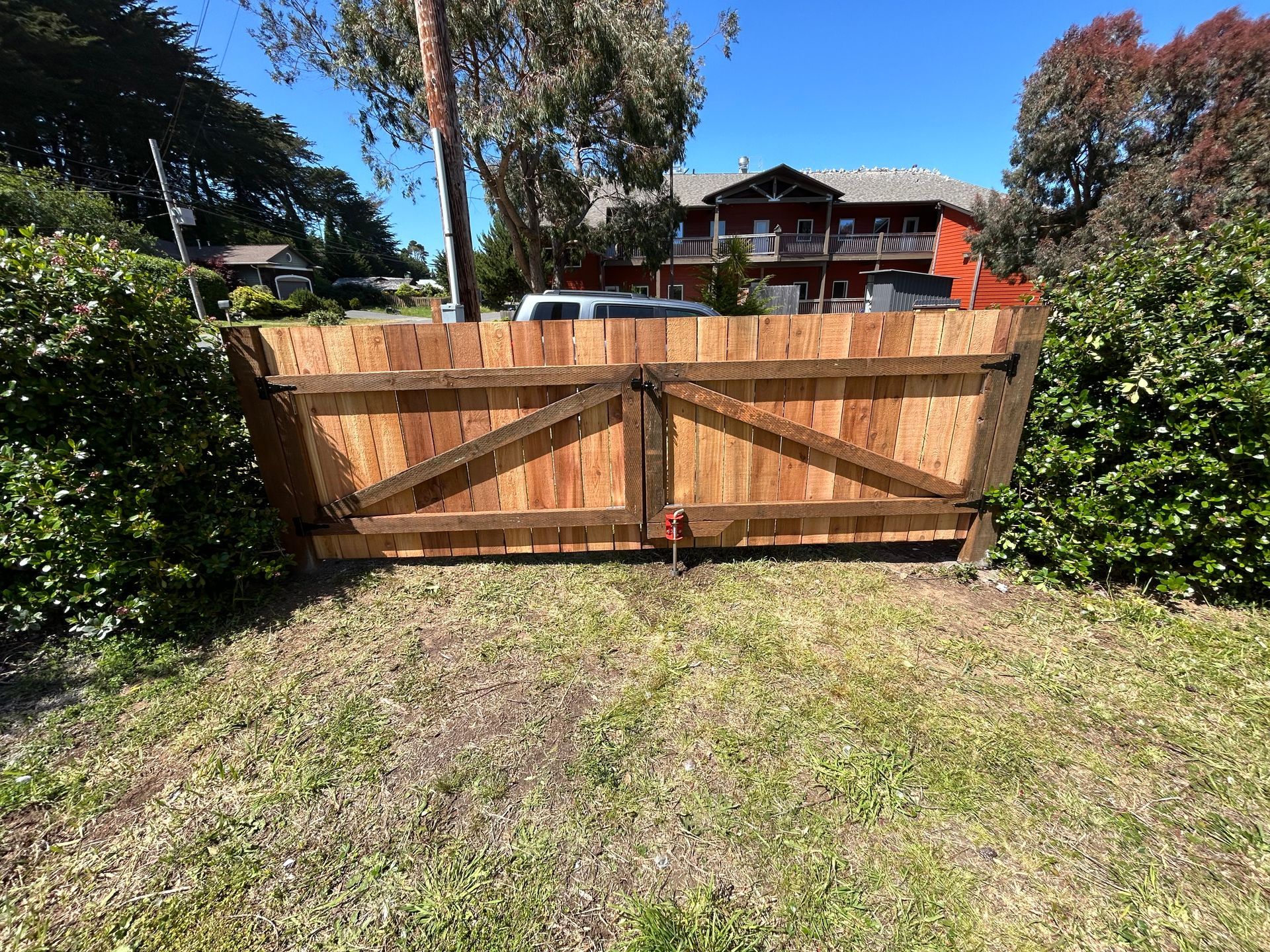 A wooden gate is sitting in the middle of a grassy field in front of a house.