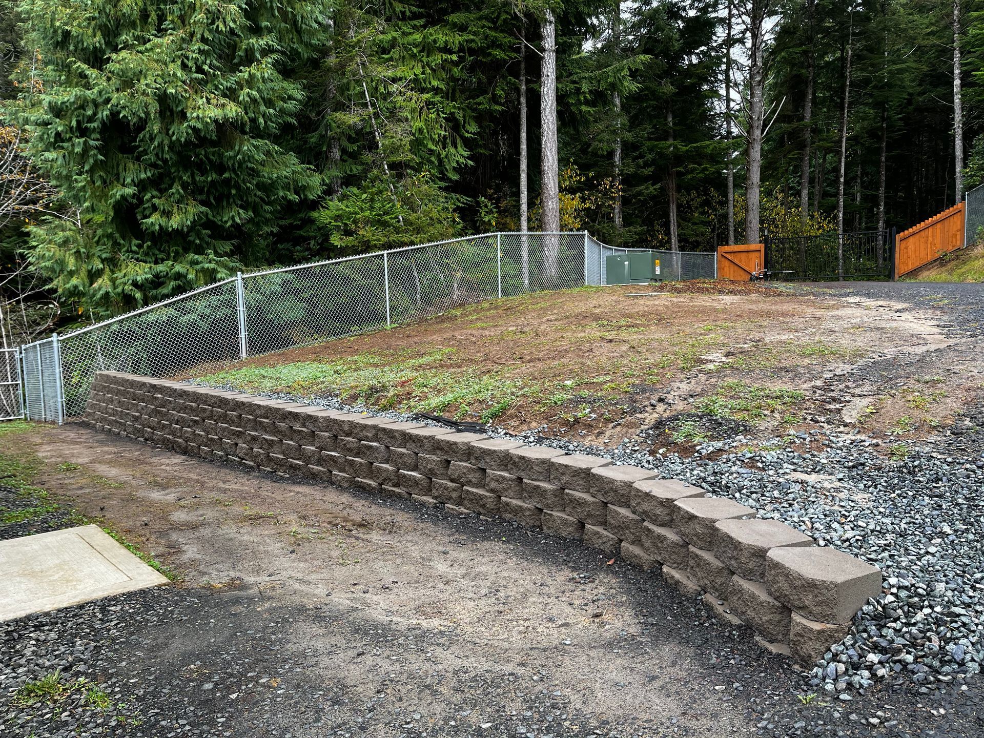 A stone wall is surrounded by gravel and a chain link fence.