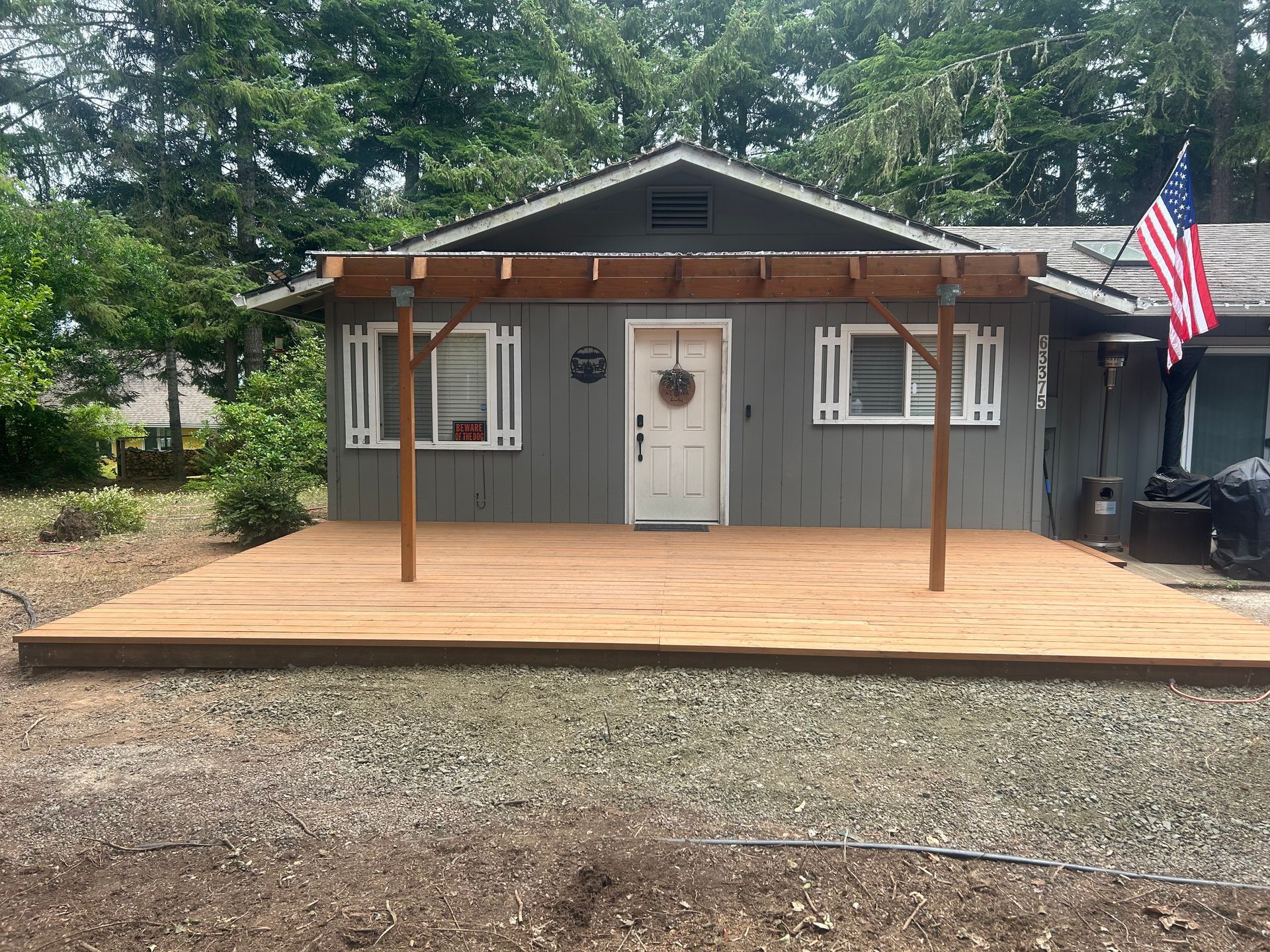 Gray house with a wooden front deck, white door, and an American flag hanging on the right.