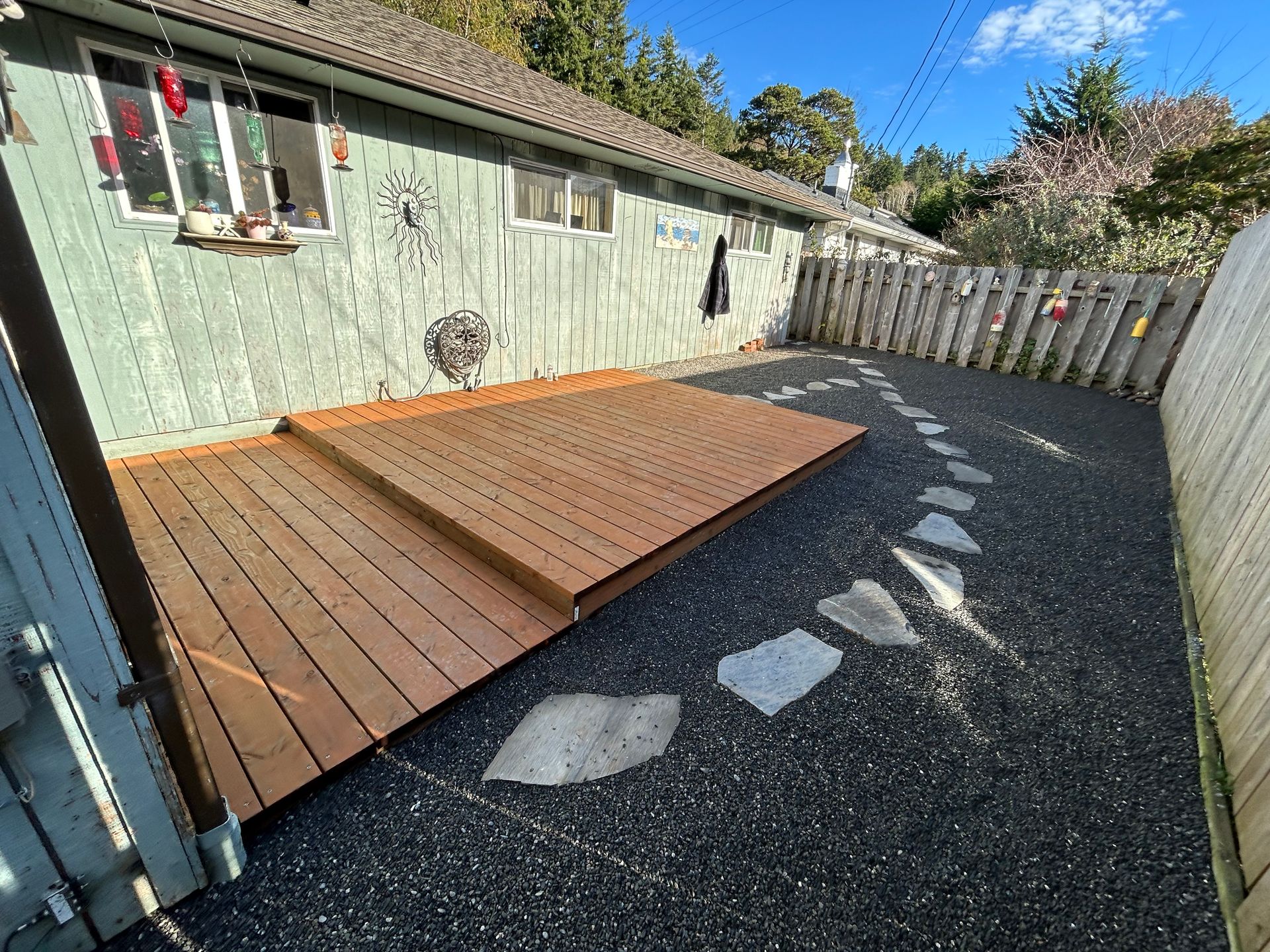 Small backyard with raised wooden deck on gravel beside a green shed and white fence.