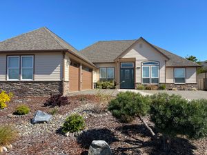 Single-story beige house with stone accents and a landscaped front yard under a clear blue sky