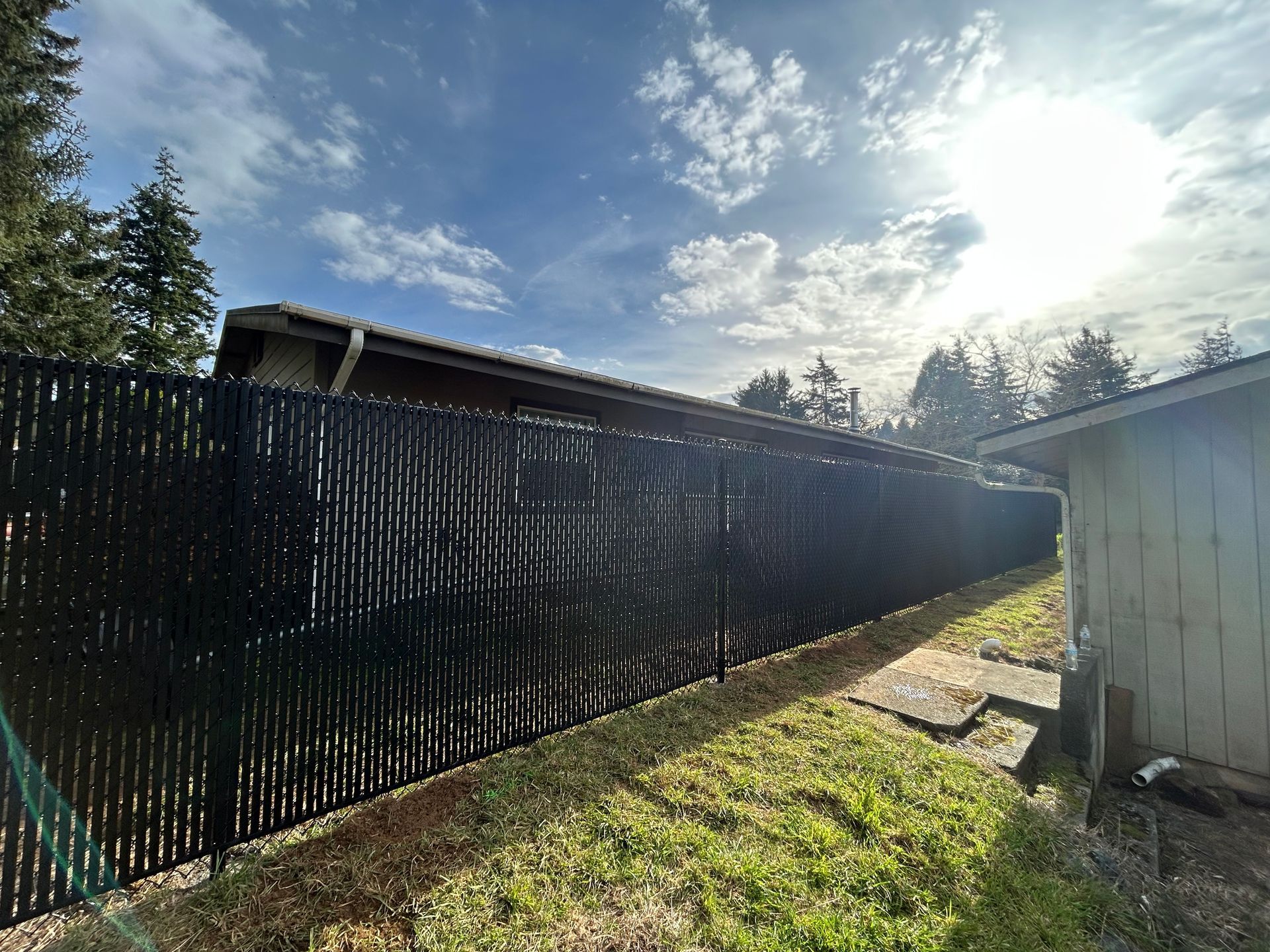 Backyard with tall black privacy fence, white shed, and bright sunny sky