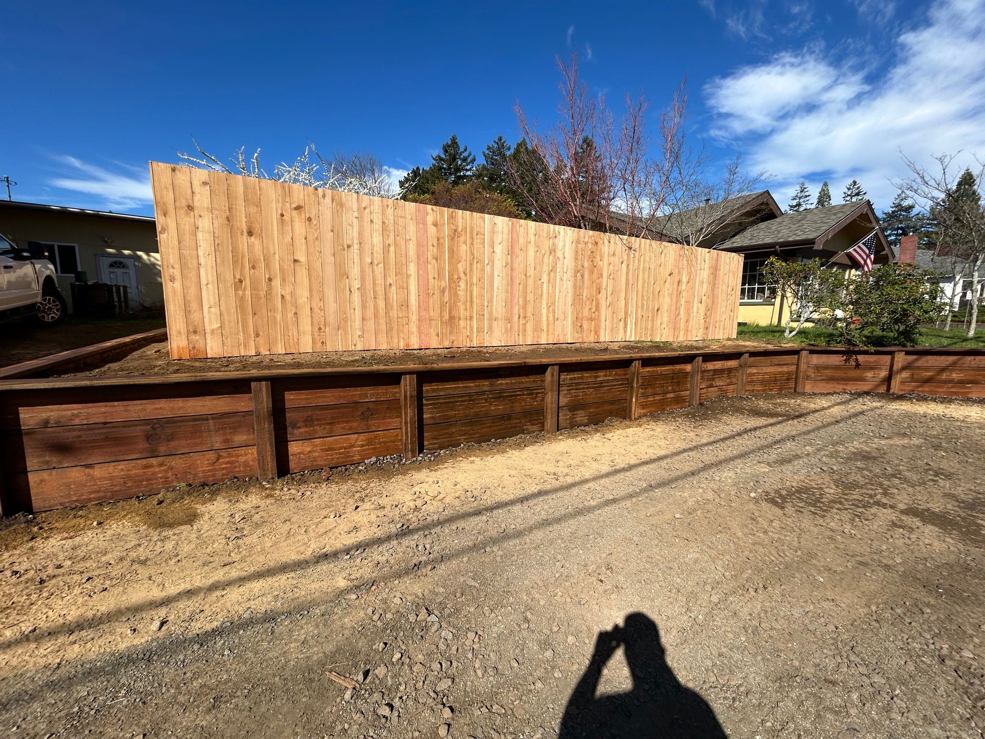 Wooden fence panel along a gravel driveway beside a house under a blue sky