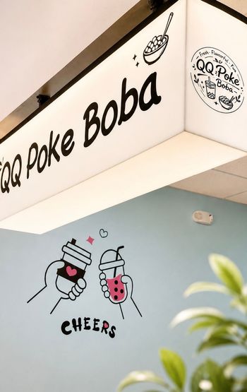 Poke boba shop sign with cartoon drinks and “CHEERS” mural on a white wall
