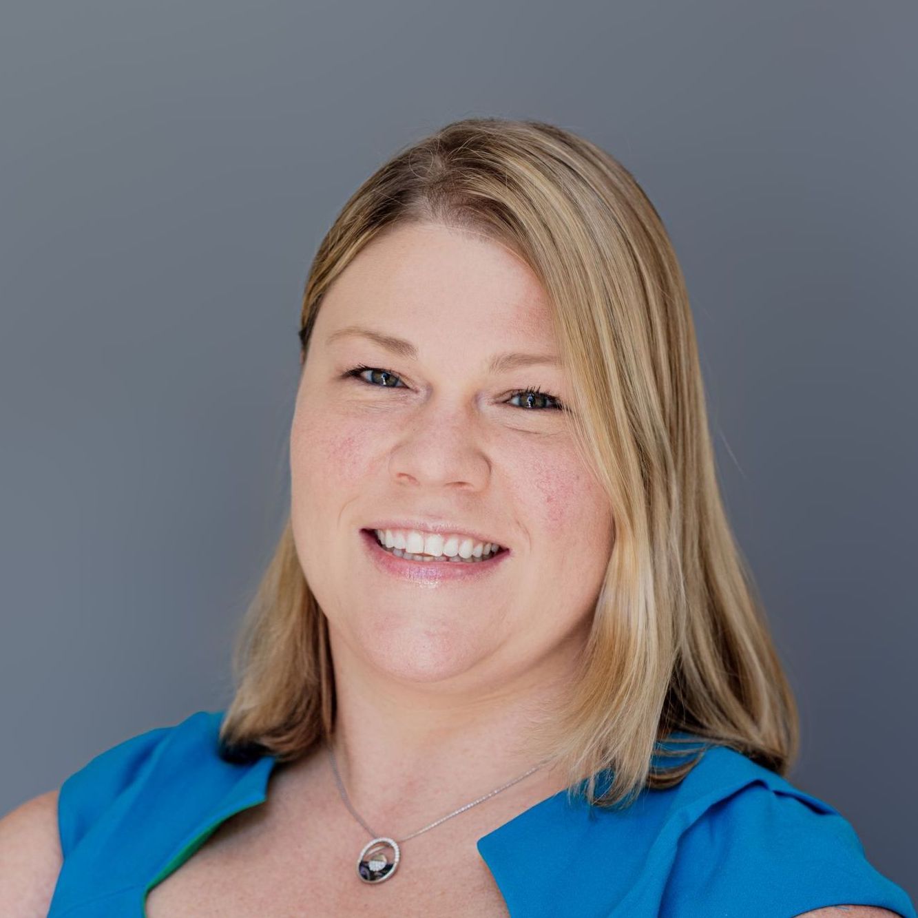 A woman in a blue dress and necklace is smiling for the camera.