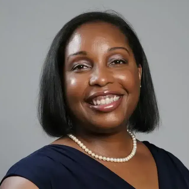 a woman wearing a pearl necklace and a blue dress is smiling .