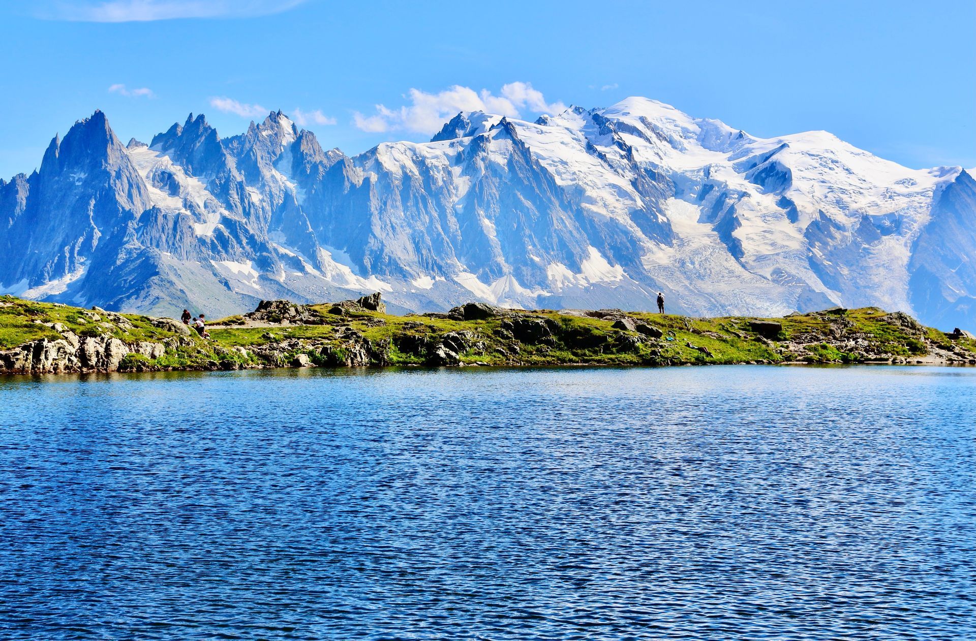 Snowy mountains beyond a blue lake and rocky shoreline under a clear sky