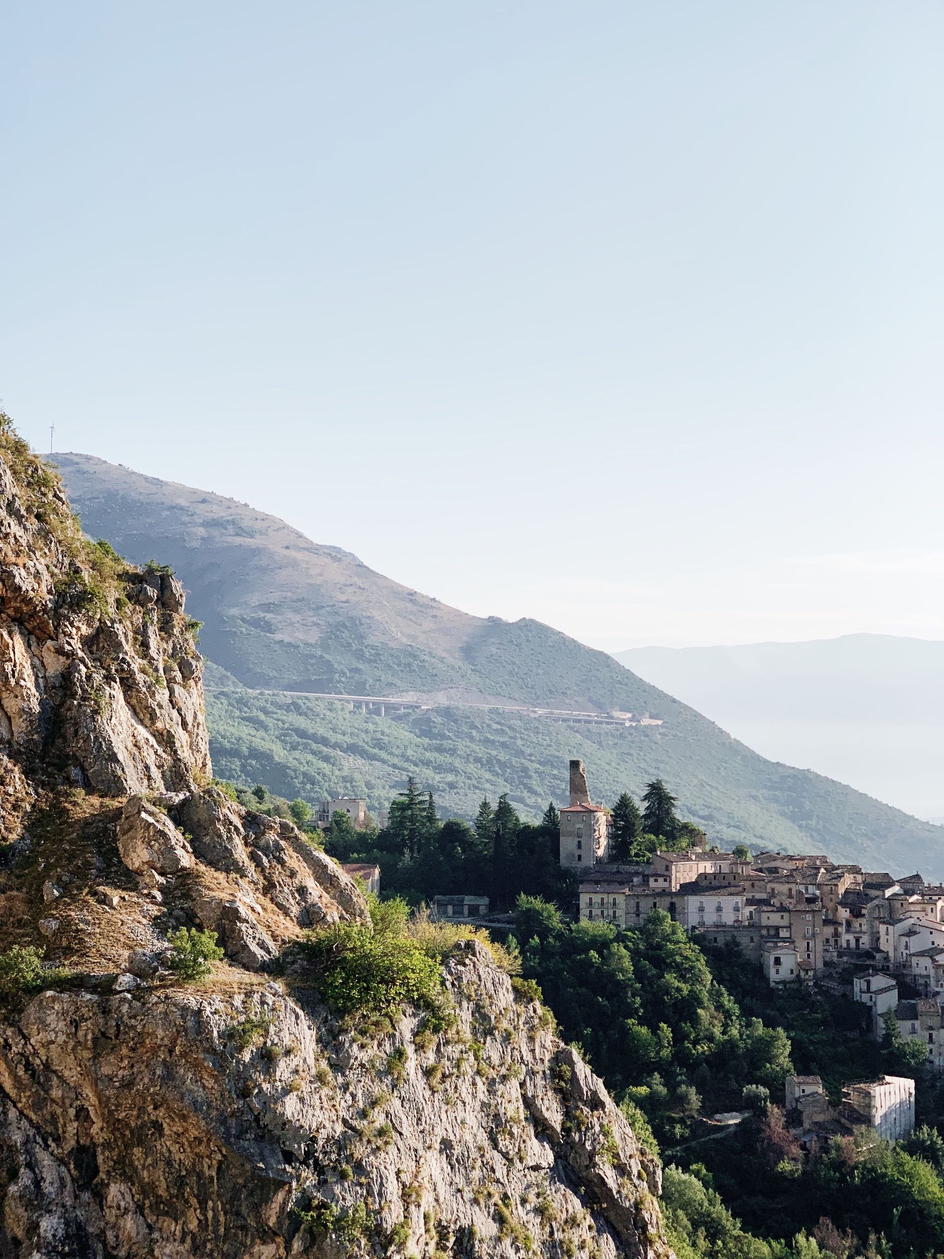 Rocky hillside overlooking a village with a church and distant green mountains under a clear sky
