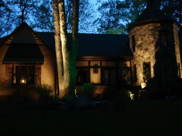 House at night, stone turret and walls lit by warm lights against a dark blue sky.
