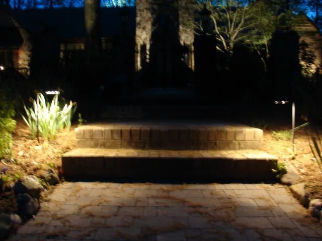 Stone steps and walkway leading to a house at night, lit by spotlights.