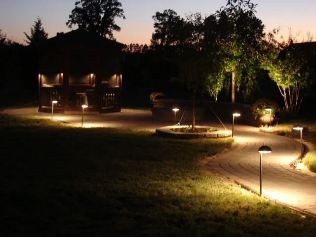 Nighttime garden with path lights leading to a gazebo, illuminated by warm light.