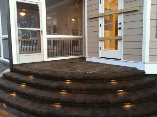 Brick steps with built-in lights lead up to a doorway and screened porch.