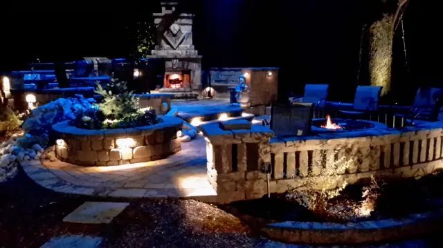 Outdoor stone patio with fire features and lighting at night.