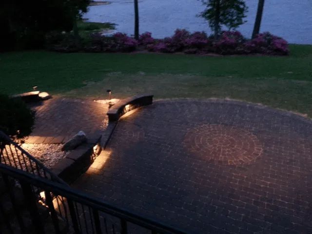 Brick patio with landscape lighting at dusk, overlooking a lake with pink flowers.